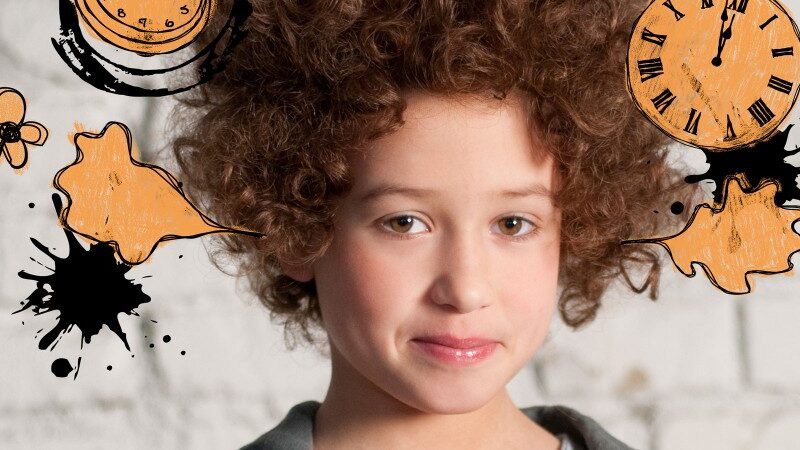 Ein Kind mit lockigem Haar steht vor einer weißen Backsteinmauer, um seinen Kopf herum sind Abbildungen von Uhren, Blumen und Farbspritzern digital hinzugefügt.