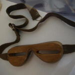 Eine Schneebrille aus Holz mit zwei schmalen Augenschlitzen und einem verstellbaren Stoffband.