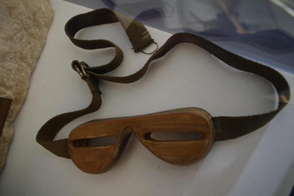 Eine Schneebrille aus Holz mit zwei schmalen Augenschlitzen und einem verstellbaren Stoffband.