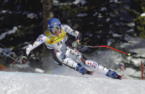 Ein Skifahrer im Rennanzug und mit Helm macht eine scharfe Kurve auf einer verschneiten Abfahrtspiste während eines alpinen Skirennens.