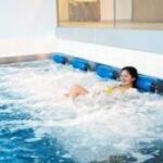 Eine Frau entspannt sich in einem Hallenbad mit sprudelnden Wasserdüsen an der Beckenwand.