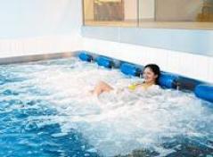 Eine Frau entspannt sich in einem Hallenbad mit sprudelnden Wasserdüsen an der Beckenwand.