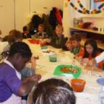 Eine Gruppe von Kindern sitzt um einen Tisch in einem Klassenzimmer und beschäftigt sich mit verschiedenen Bastelmaterialien.