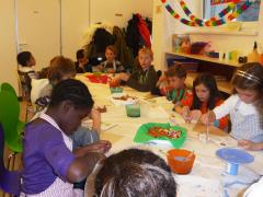 Eine Gruppe von Kindern sitzt um einen Tisch in einem Klassenzimmer und beschäftigt sich mit verschiedenen Bastelmaterialien.