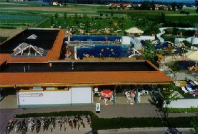 Luftaufnahme eines Freibadkomplexes mit schwimmenden und sonnenbadenden Menschen und Fahrrädern, die in der Nähe des Eingangs abgestellt sind.