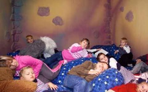 In einem Raum mit bemalten Steinwänden liegen und faulenzen mehrere Kinder auf einem Stapel von blauen Kissen.