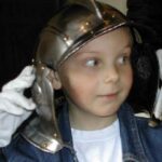 Ein Kind, das einen Metallhelm und weiße Handschuhe trägt, schaut zur Seite.