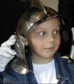 Ein Kind, das einen Metallhelm und weiße Handschuhe trägt, schaut zur Seite.