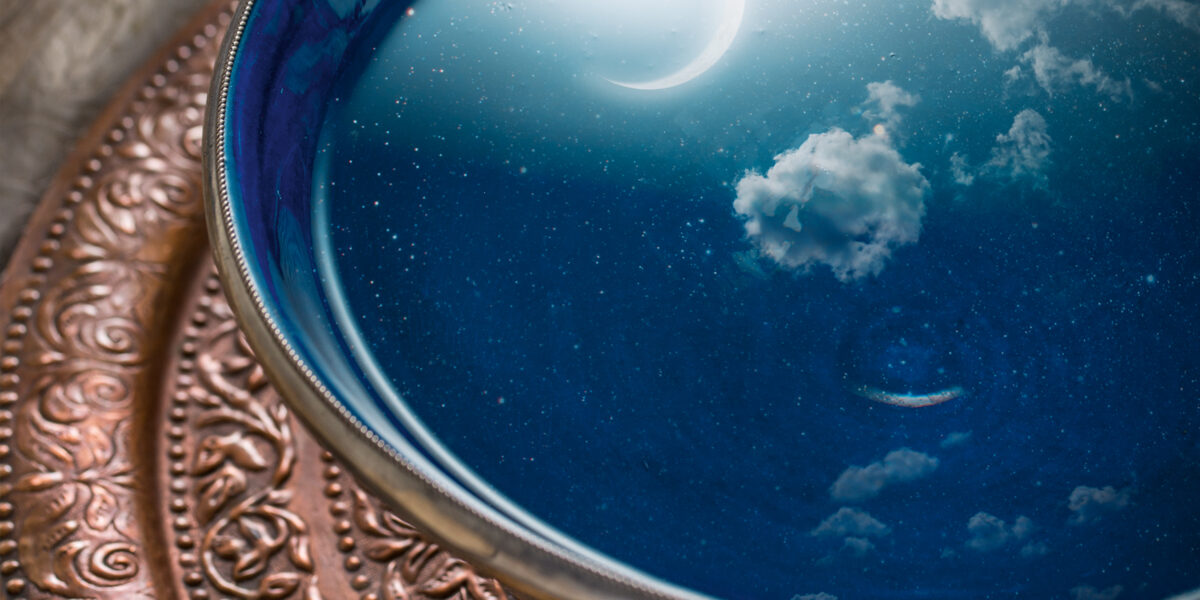 In einer blauen Schale mit Wasser auf einem verzierten Metalltablett spiegeln sich eine Mondsichel und Wolken, so dass in der Schale die Illusion eines Nachthimmels entsteht.