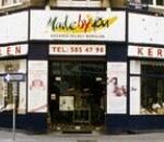 Straßeneckenansicht eines Keramikgeschäfts mit großen Fenstern und einem Schild mit der Aufschrift "Malen XL Keramik Selber Bemalen". Zwei Personen stehen in der Nähe des Eingangs.