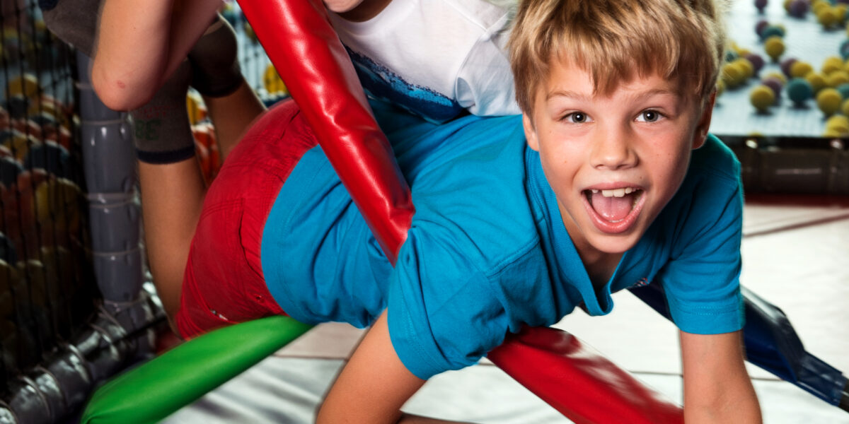 Zwei kleine Jungen spielen und lächeln, während sie auf bunten gepolsterten Stangen in einem Indoor-Spielbereich klettern.