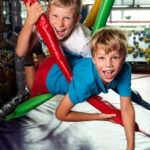 Zwei kleine Jungen spielen und lächeln, während sie auf bunten gepolsterten Stangen in einem Indoor-Spielbereich klettern.