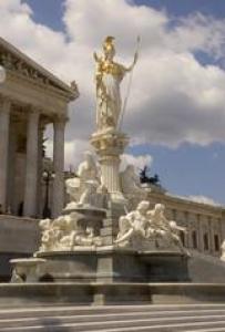 Die Athena-Statue steht auf einem Brunnen vor dem österreichischen Parlamentsgebäude, mit neoklassizistischer Architektur und bewölktem Himmel im Hintergrund.