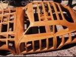 Holzgerüst einer Autokarosserie auf einer gepflasterten Fläche, das die strukturellen Umrisse und das Design des Fahrzeugs zeigt.