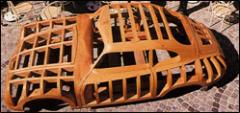Holzgerüst einer Autokarosserie auf einer gepflasterten Fläche, das die strukturellen Umrisse und das Design des Fahrzeugs zeigt.