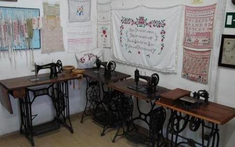 Drei alte Nähmaschinen stehen nebeneinander an einer Wand, die mit bestickten Stoffen und Mustertüchern dekoriert ist.