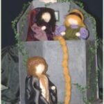 Drei handgefertigte Puppen stellen das Märchen von Rapunzel dar. Eine Puppe befindet sich in einem Turm und lässt ihr langes gelbes Haar auf eine darunter stehende Figur und eine weitere Figur neben ihr herab.