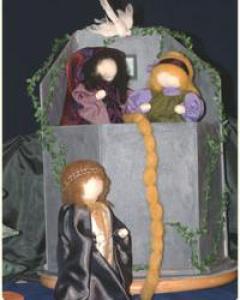 Drei handgefertigte Puppen stellen das Märchen von Rapunzel dar. Eine Puppe befindet sich in einem Turm und lässt ihr langes gelbes Haar auf eine darunter stehende Figur und eine weitere Figur neben ihr herab.