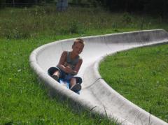 Ein kleines Kind sitzt auf einer von Gras umgebenen Betonrutsche und schaut nach vorne, während es sich an den Knien festhält.