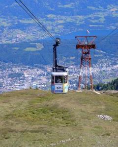 Eine Seilbahn fährt einen grasbewachsenen Berghang hinauf, während im Hintergrund eine Stadt und eine Landschaft zu sehen sind.