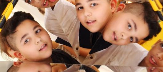 Drei Kinder sind mehrfach in einer Spiegelung zu sehen, wodurch ein fragmentierter visueller Effekt entsteht.