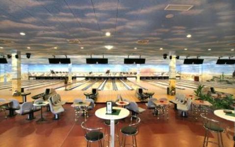Eine moderne Bowlingbahn mit mehreren Bahnen und Overhead-Bildschirmen, mit Sitzbereichen mit Stühlen und Tischen im Vordergrund.