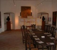 Ein Konferenzraum mit einem langen Tisch, Holzstühlen, Dokumenten auf dem Tisch, Kunstwerken an den Wänden und zwei Büstenskulpturen auf Sockeln.