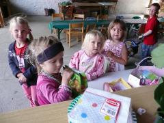 Fünf kleine Kinder sitzen um einen Tisch mit Snacks und Spielzeug in einer lockeren Innenumgebung mit Stühlen und Tischen im Hintergrund.