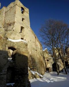Eine hohe Steinruine steht im Sonnenlicht, teilweise mit Schnee bedeckt, mit blattlosen Bäumen und tiefblauem Himmel im Hintergrund.