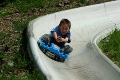 Ein Kind fährt an einem sonnigen Tag im Freien auf einem blauen Schlitten eine Betonrutsche hinunter.