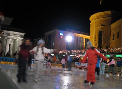 Kinder, die nachts im Freien Schlittschuh laufen, mit beleuchteten Gebäuden im Hintergrund.