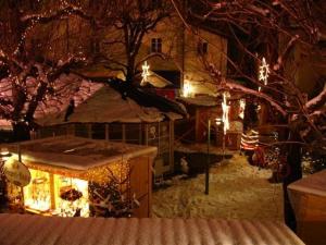 Ein verschneiter Markt im Freien bei Nacht, beleuchtet von Lichterketten und dekorierten Ständen, mit kahlen Bäumen und schneebedecktem Boden.