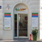 Schaufenster mit einer Glastür unter einem Bogenfenster, flankiert von bunten Schildern mit der Aufschrift "Made by You", an einem weißen Backsteingebäude an einer Straßenecke.