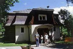 Eine kleine Gruppe von Menschen steht an einem sonnigen Tag vor einem malerischen Gebäude im Landhausstil, umgeben von Bäumen und Grünflächen.