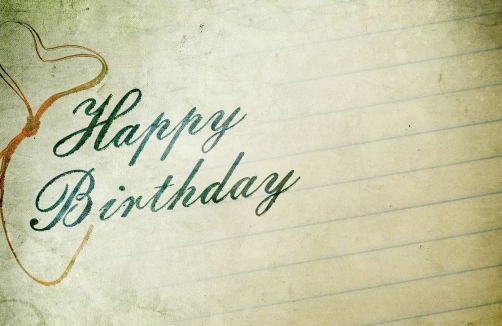 Eine Karte im Vintage-Stil mit liniertem Papierhintergrund und "Happy Birthday" in kursiver grüner Schrift. Eine braune Schleife und ein Herz sind auf der linken Seite zu sehen.