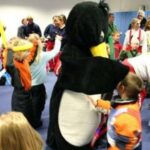 Kinder und Erwachsene versammeln sich im Haus und spielen um eine Person in einem großen Pinguinkostüm.