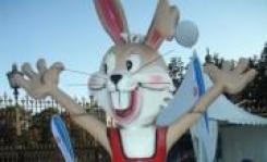 Große Cartoon-Kaninchen-Statue mit erhobenen Armen, in rotem Outfit, im Freien in der Nähe eines weißen Zeltes und eines Metallzauns.