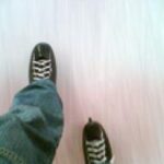 Eine Person in dunklen Schlittschuhen und blauen Jeans, die auf einer Eisbahn Schlittschuh läuft.