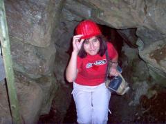 Eine Person, die einen roten Schutzhelm und ein rotes Hemd trägt, geht mit einer Taschenlampe in der Hand durch einen engen, felsigen Tunnel.