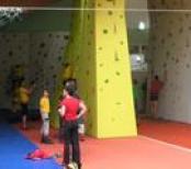 Mehrere Kinder und Erwachsene nehmen am Indoor-Klettern an den bunten Kletterwänden in einer Sporthalle teil.