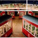 Mehrere rote, nummerierte Kabinen mit Fenstern sind kreisförmig auf einem Holzboden unter einer mit gemalten Szenen verzierten Kuppel angeordnet.