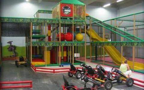 Indoor-Spielplatz mit Klettergerüsten, Rutschen, Softplay-Bereich und mehreren Tret-Go-Karts; ein Erwachsener sitzt in der Nähe.