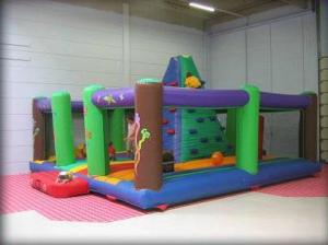 Aufblasbares Indoor-Spielgerät mit Kletterwand und bunten Säulen auf einem rot-weiß karierten Boden in einem geräumigen Raum.