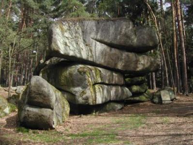 Große, geschichtete Felsformation in einem bewaldeten Gebiet mit Moos und Bäumen im Hintergrund.
