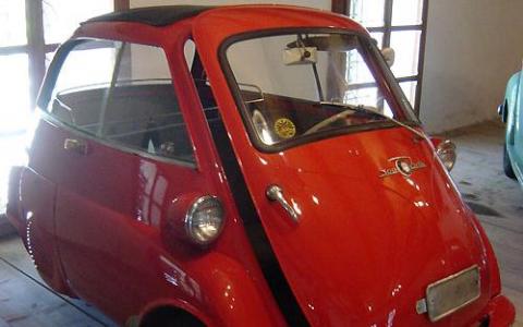 Ein roter BMW Isetta Kleinwagen mit einer einzigen Vordertür ist in der Nähe von Fenstern geparkt.