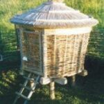 Ein kleines, rundes, strohgedecktes Gebäude aus geflochtenen Ästen, das auf Holzpfählen steht und zu dessen Eingang eine kurze Leiter führt.