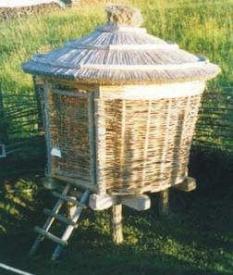 Ein kleines, rundes, strohgedecktes Gebäude aus geflochtenen Ästen, das auf Holzpfählen steht und zu dessen Eingang eine kurze Leiter führt.