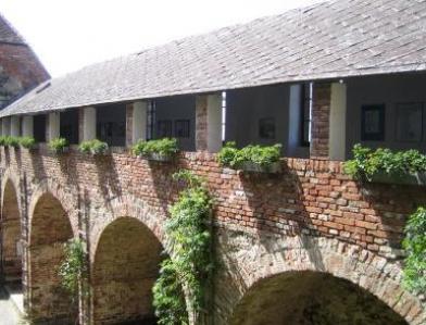 Eine gemauerte Arkade mit Bögen und einem überdachten Gang darüber, mit Säulen und Grünpflanzen auf der oberen Ebene.