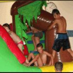 Mehrere Kinder in Badeanzügen spielen auf einer aufblasbaren Wasserrutsche in einer Halle.