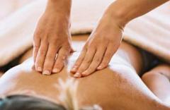 Person, die eine Rückenmassage erhält, wobei zwei Hände den nackten, teilweise mit einem Handtuch bedeckten oberen Rücken drücken und massieren.